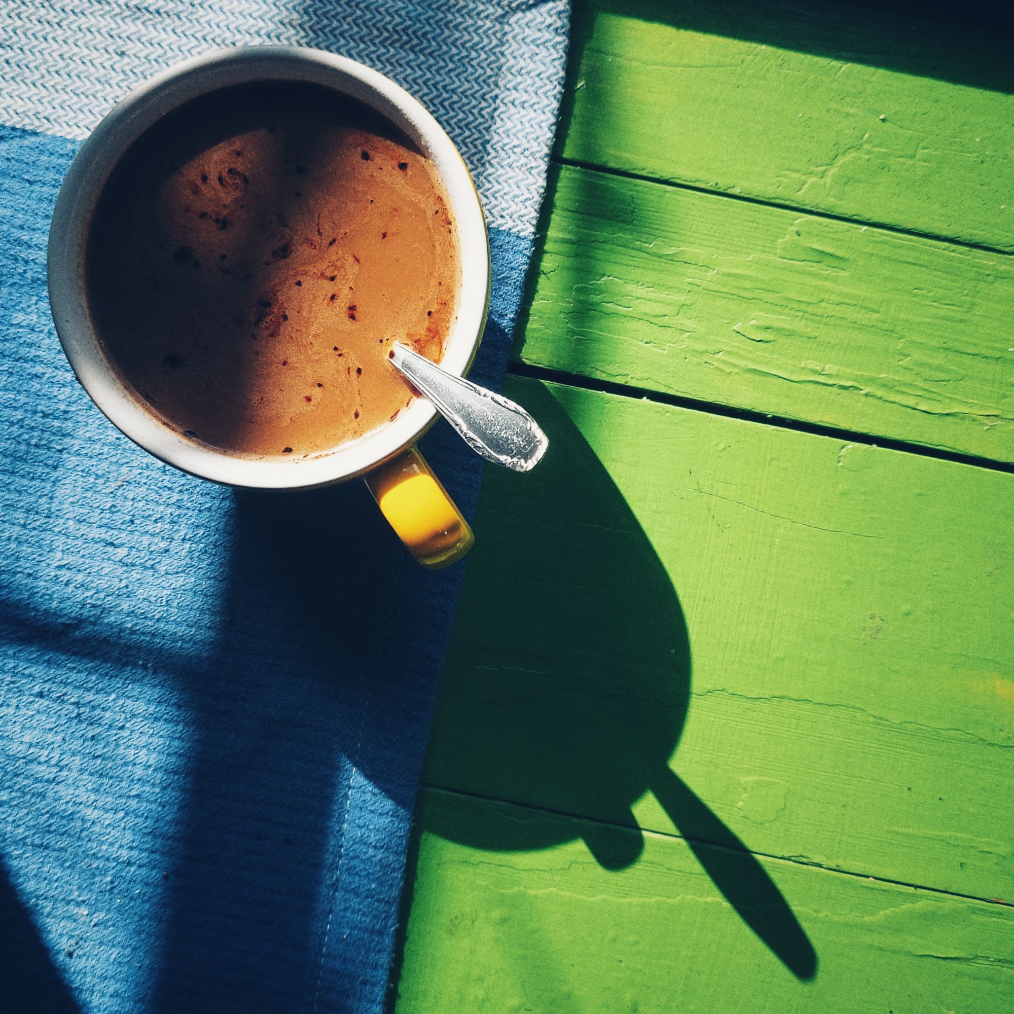 A coffee cup casting shadow on a board of green wood.