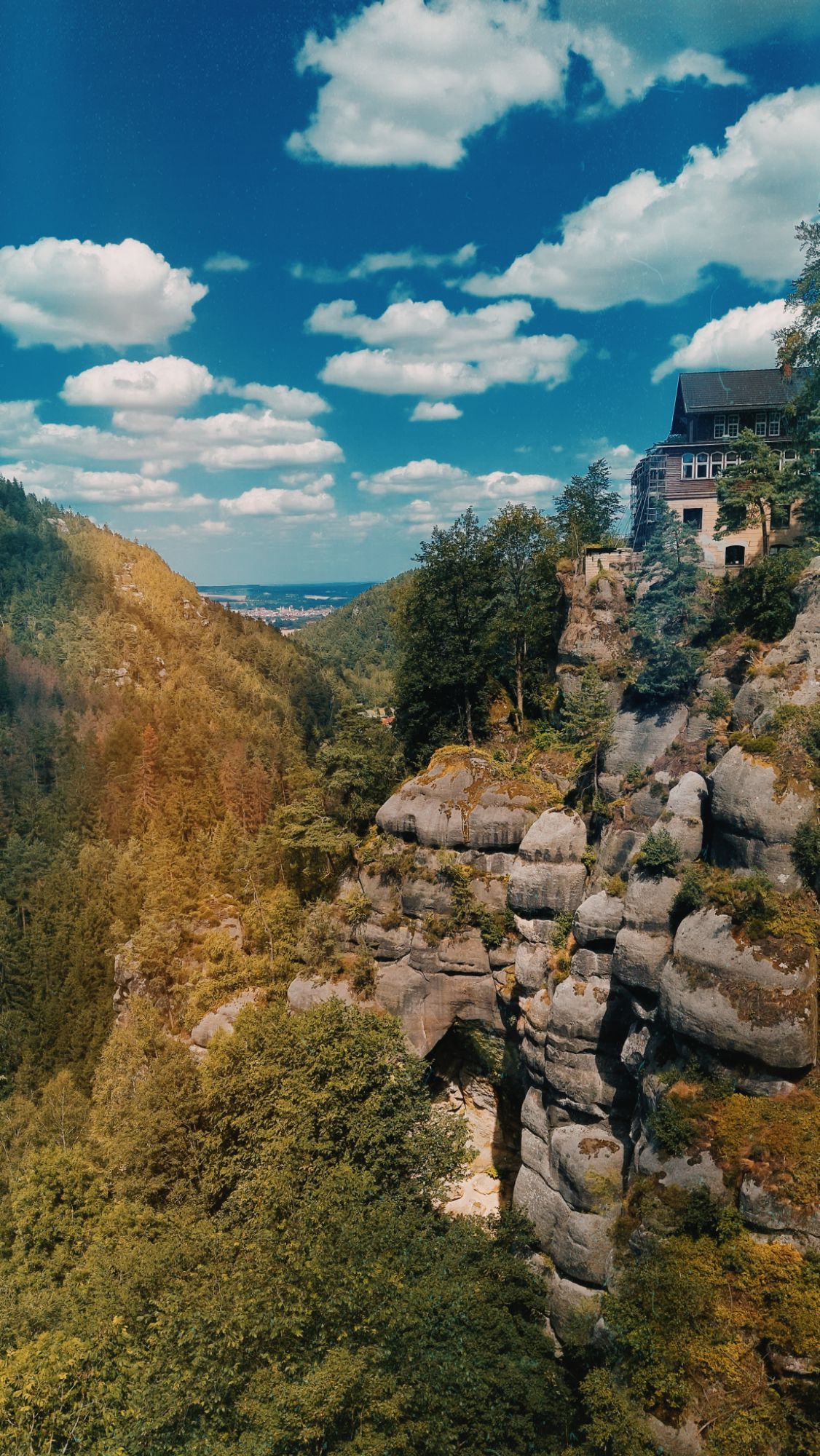 Countryside under blue sky. Steep rocks covered with trees, and a house on the top.