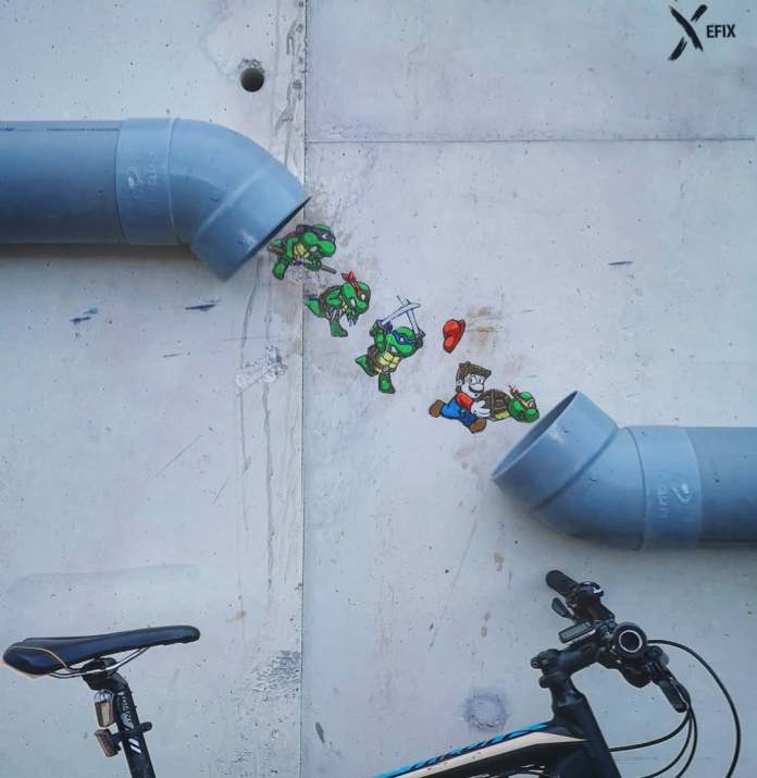 A street art creation by EFIX featuring the Teenage Mutant Ninja Turtles and Mario from Super Mario Bros. cleverly interacting with two gray pipes on a wall. The turtles appear to be sliding down the left pipe, chasing Mario, who is leaping toward the right pipe. The playful design merges the characters with the urban setting, creating a dynamic and humorous scene. A bicycle is partially visible at the bottom, adding another layer to the urban environment.