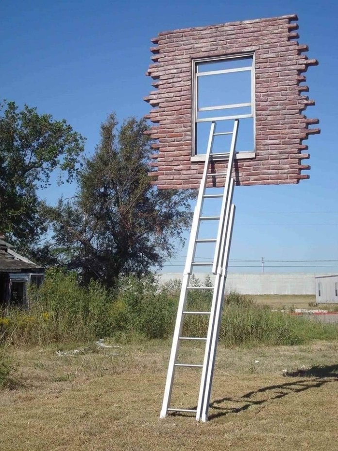 A surreal sculpture features a tall white ladder leading to a brick wall with an open window, floating above a field under a clear blue sky, creating an illusion of mystery and imagination.