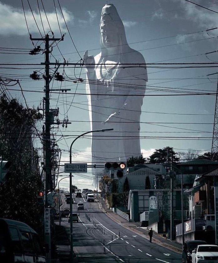 View of the towering Sendai Daikannon statue in Sendai, Japan, framed against a city street with power lines and traffic lights in the foreground. The statue, at 100 meters (330 ft) tall, is the eighth-tallest statue in the world. Its serene, watchful presence overlooks the quiet urban landscape, creating a striking contrast between its massive spiritual form and the everyday city life below.