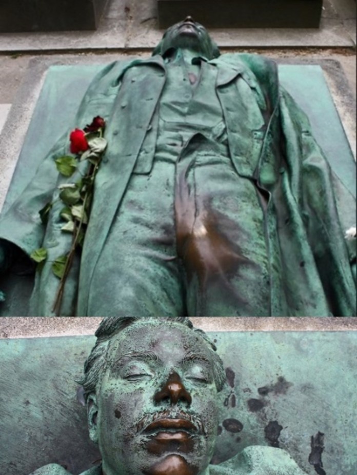 Victor Noir’s grave in Père-Lachaise Cemetery, a life-sized bronze sculpture depicting the journalist lying on his back, created by Patrick Magaud in 1984. The statue shows Noir as if recently fallen, with a rose placed on his coat. Over time, parts of the sculpture, particularly his lips and the bulge on his trousers, have become shiny due to a tradition where visitors rub or kiss these areas for good luck, fertility, or to improve their love lives. This unusual practice has made Victor Noir’s grave one of the most visited sites in the cemetery, steeped in legend and local lore.