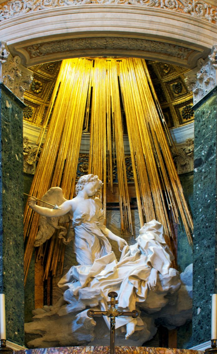 The Ecstasy of Saint Teresa, a renowned Baroque sculpture by Gian Lorenzo Bernini, located in the Cornaro Chapel of Santa Maria della Vittoria in Rome. This intricate marble sculpture depicts Saint Teresa of Ávila in a moment of religious ecstasy, her face expressing both pain and bliss as an angel holds a golden spear poised above her. Radiant golden rays crafted from gilded bronze descend from above, symbolizing divine light and adding dramatic intensity to the scene. The combination of marble and golden rays exemplifies Bernini's skill in blending materials to create a dynamic, spiritual experience for viewers.
