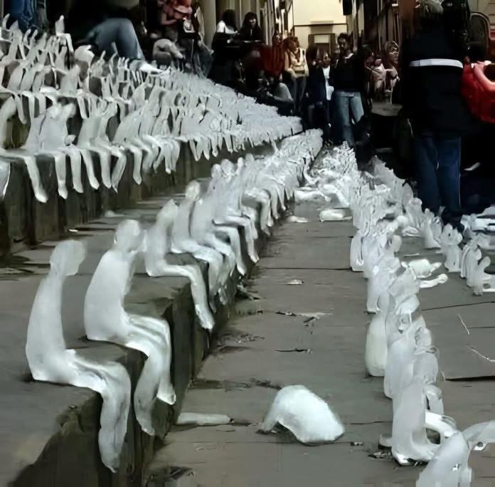 Rows of tiny ice figurines shaped like human figures are placed on the steps of Gendarmenmarkt square in Berlin, Germany, as part of Nele Azevedo’s public art installation. The melting sculptures symbolize the rapid effects of global warming and draw attention to the fragility of life in the face of climate change. The installation, organized with WWF Germany, emphasizes the urgent need to address the climate crisis. A crowd of onlookers observes the powerful display.