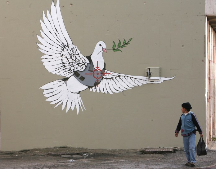 Banksy's mural 'Armored Peace Dove' depicting a white dove in a bulletproof vest targeted by crosshairs, holding an olive branch, located in Bethlehem, Palestine.