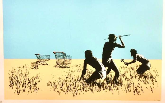 'Trolleys' by Banksy from the Barely Legal show in Los Angeles, USA, 2006. This artwork features three silhouetted hunter-gatherer figures crouching in tall grass, armed with spears and sticks, as they appear to stalk two abandoned shopping carts in the distance. The juxtaposition of primitive hunting tactics with modern shopping carts creates a satirical commentary on consumerism and its impact on society. The blue sky and beige ground emphasize the barren setting, enhancing the surreal and ironic nature of the scene.