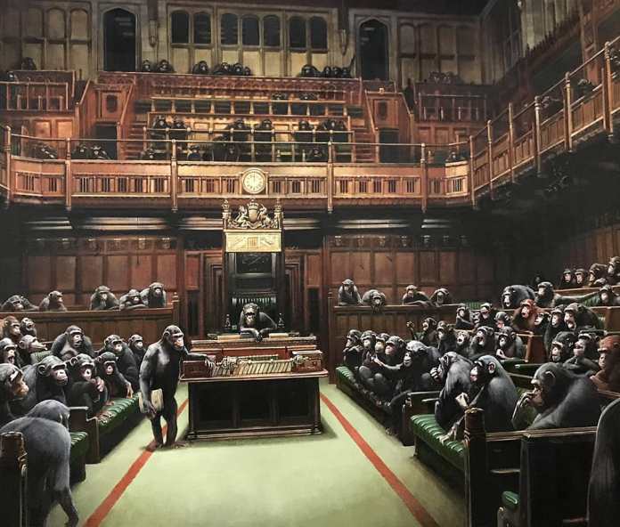 'Devolved Parliament,' a painting by Banksy displayed at the Banksy vs. Bristol Museum exhibition in 2009. The artwork depicts the British House of Commons, but instead of human politicians, the seats are filled with chimpanzees engaged in debate and discussion. The detailed rendering of the historical chamber contrasts with the satirical portrayal of apes in place of members of parliament, suggesting a critique of political discourse. The scene is both humorous and thought-provoking, raising questions about governance, representation, and the nature of political power.