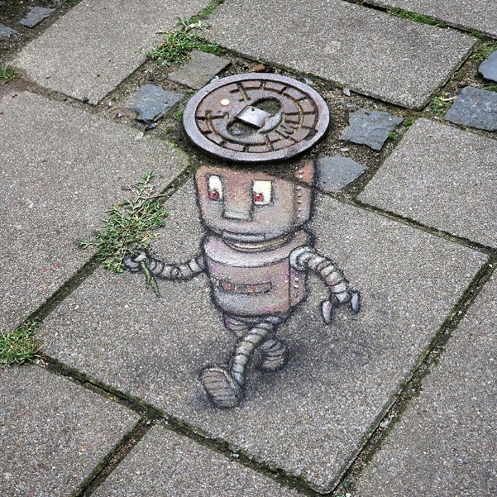 A whimsical chalk art creation by David Zinn features a cute robot strolling across a paved surface. The robot’s head is cleverly integrated with a real metal manhole cover, adding a 3D illusion to the piece. Its mechanical body is detailed with bolts and rivets, and it holds a small bouquet of greenery in one hand, creating a humorous and endearing contrast. The artwork is framed by the uneven textures of the pavement and scattered patches of grass, showcasing Zinn’s signature integration of art with the environment.