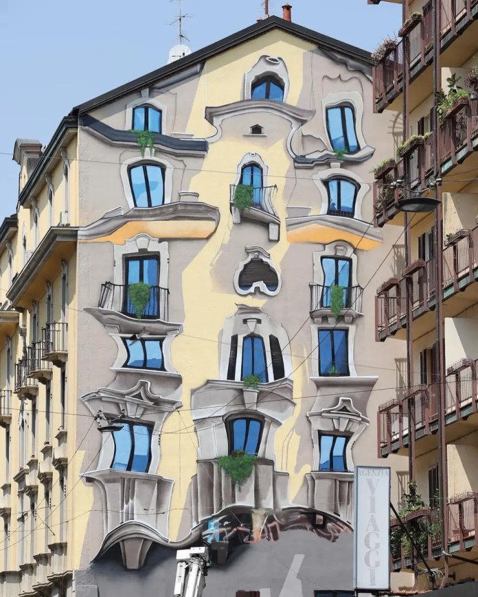 Mural by artist Cosimo Cheone Caiffa on a building facade in Milan, Italy, featuring a surreal, distorted architectural illusion. The artwork depicts a traditional building facade that appears to melt and warp, with windows and balconies bending in unusual directions. The vibrant blue windows and exaggerated curves create an optical illusion, as if the building's structure is fluid and bending under pressure. The surrounding buildings with standard facades emphasize the striking effect of the mural, adding a playful and whimsical touch to the urban landscape.