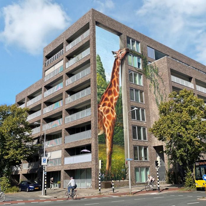 Wide-angle shot of the multi-story residential building featuring Jan Is De Man's giraffe mural in Utrecht, Netherlands, highlighting the urban surroundings and the mural's integration with the neighborhood.