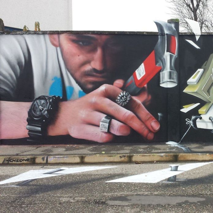 A hyper-realistic 3D mural by Cosimo Cheone Caiffa showing a man intensely focused on using a red hammer. The man’s hand, adorned with a detailed wristwatch and silver rings, appears to emerge from the wall, creating the illusion of breaking into the viewer’s space. The vivid details, including the texture of his skin and the reflective surfaces of the hammer, blend seamlessly with the environment. The inclusion of the pavement in the composition enhances the trompe-l'œil effect, making this a remarkable example of Cheone's mastery in optical illusion art.