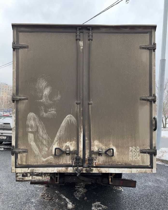Grime art by ProBoyNick (Nikita Golubev) on the back of a truck, depicting a ghostly, skeletal figure in a seated, curled-up position. The haunting image is skillfully scratched into the dirt on the truck's surface, creating a striking contrast between the figure and the grimy background. ProBoyNick’s artwork turns the mundane surface of the truck into an evocative, temporary piece of art.
