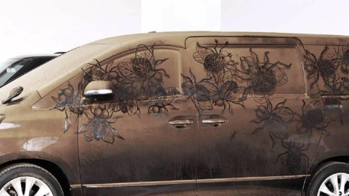 Grime art on the side of a van, featuring a detailed swarm of large insects, including flies, etched into the dirt covering the vehicle’s surface. The intricate designs use the van’s grime as a canvas, creating a striking, textured effect as the insects appear to crawl across the vehicle’s body. This imaginative artwork turns an ordinary, dusty van into a compelling display of creativity.