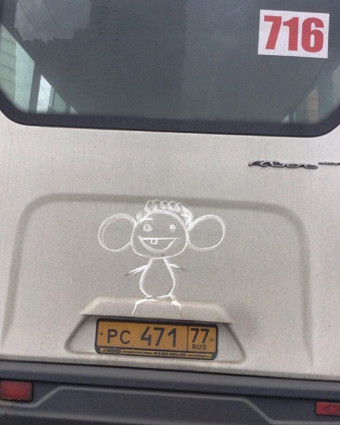 A simple grime art drawing on the back of a dusty van, featuring a cute cartoon character with large round ears, a single tooth, and a curly tuft of hair. The playful, childlike sketch stands out against the dirty surface, adding a touch of humor and personality to the vehicle.