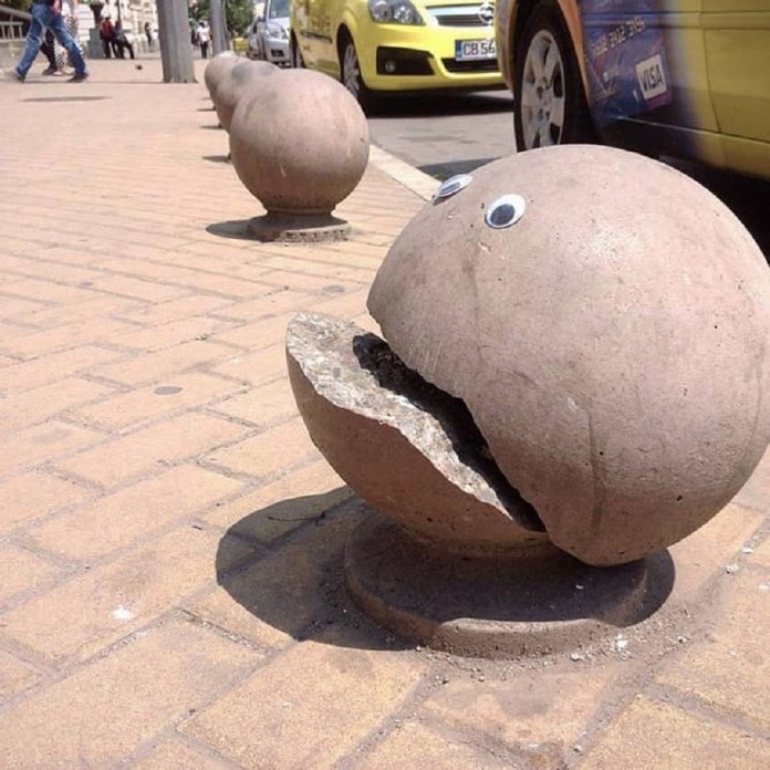 A concrete bollard on a sidewalk with a large crack resembling an open mouth, enhanced by googly eyes to look like Pac-Man.