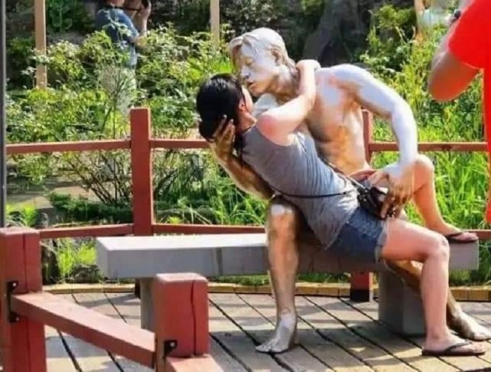 A woman sits on the lap of a statue in Love Land Sculpture Park in South Korea, leaning in as if to kiss the figure. Known for its playful and romantic sculptures, Love Land is a popular destination for visitors seeking humorous and intimate photo opportunities with its expressive statues.
