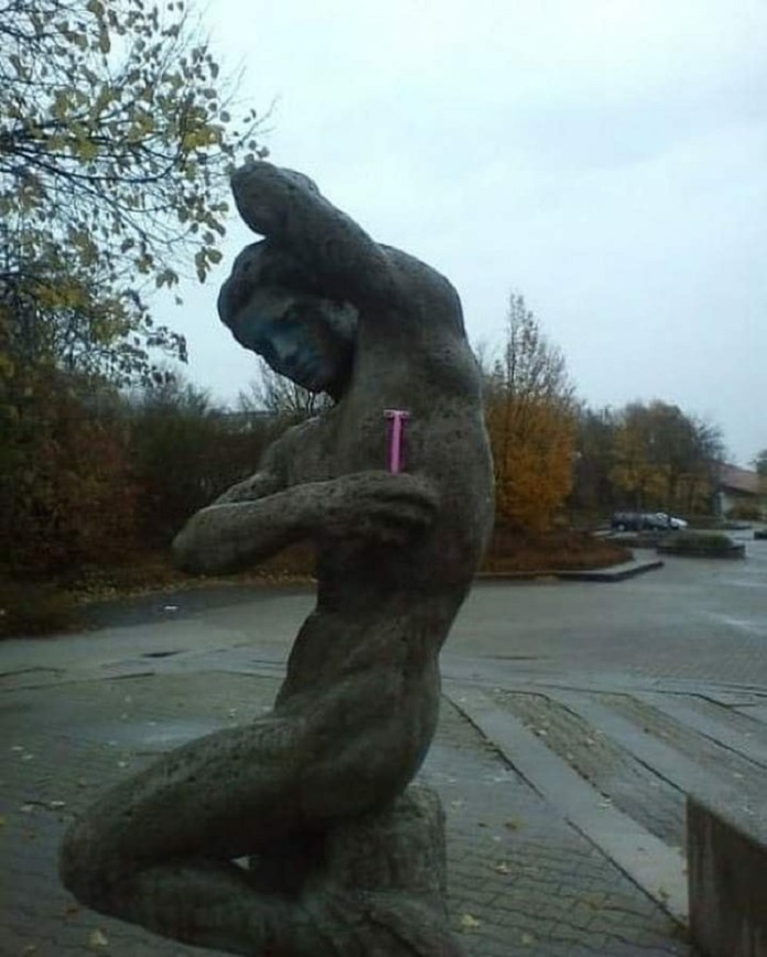 A humorous interaction with a statue: a stone figure in a classical pose, one arm raised behind its head, has been humorously altered with the addition of a pink razor placed under its armpit. The setting appears outdoors, with autumn foliage in the background. This playful intervention brings a modern twist to a traditional sculpture, making it seem as though the statue is mid-shave, creating a whimsical contrast between the timelessness of the art and the everyday modern object.