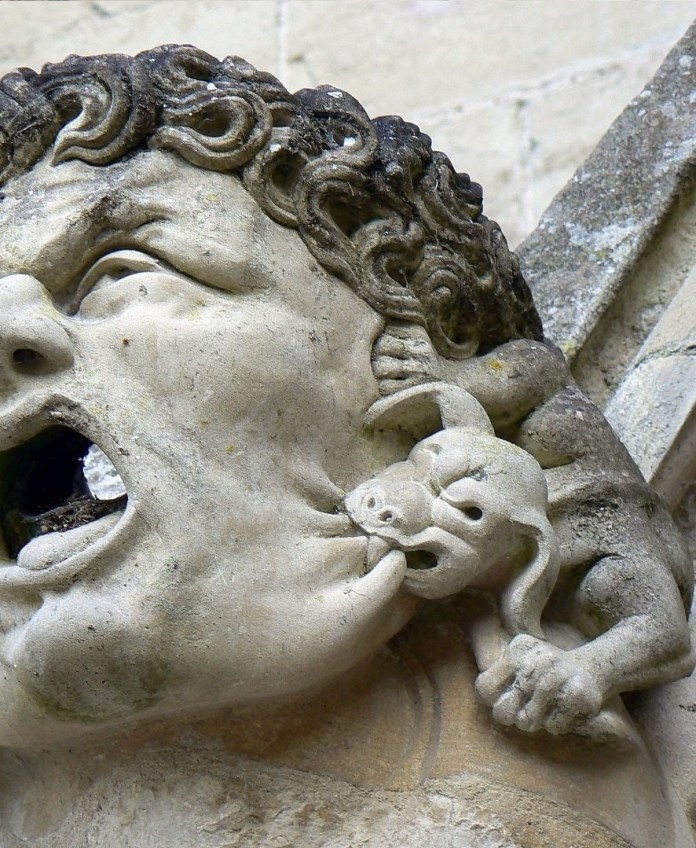 A small grotesque creature biting the ear of a larger gargoyle at the roof of Salisbury Cathedral, UK. This whimsical and humorous gargoyle is an excellent example of medieval artists' use of playful expressions in Gothic architecture, blending function as a water spout with artistic and symbolic elements.