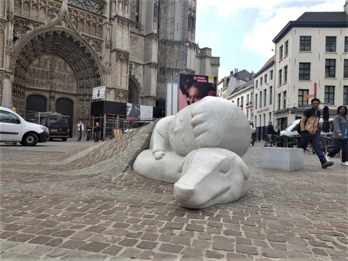 A heartwarming sculpture of Nello and Patrasche, from the novel A Dog of Flanders, lying together under a cobblestone blanket. Created by artist Batist Vermeulen (Tist), the artwork is located in Antwerp, Belgium, near the Cathedral of Our Lady. The intricate gothic cathedral facade forms a stunning backdrop, highlighting the deep connection between the characters in this poignant public artwork.