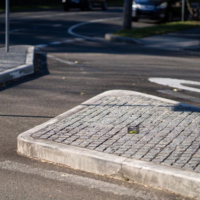 A small patch of artificial grass, enclosed by a miniature barbed wire fence with a "KEEP OUT: PRIVATE PROPERTY" sign, situated on a cobblestone island in the middle of a roadway. This piece by Michael Pederson in Sydney, Australia, humorously contrasts the fenced-off area with the open urban environment around it.
