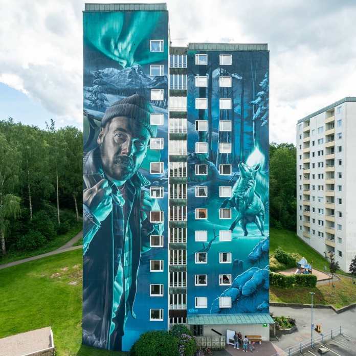Large mural by Smug in Partille, Göteborg, created for the Artscape project. The artwork is inspired by the Finnish folk tale of Revontulet, depicting the origin of the Aurora Borealis. The mural shows a bearded man dressed in winter clothing, with an intense gaze, suggesting he is the lost hiker from the tale. To the right, a majestic fox ignites the sky with the Northern Lights, illuminating the icy forest to guide the hiker. Painted in cool shades of blue and green, the mural’s vibrant Northern Lights stretch across the building's height, making it the tallest mural in Sweden, and possibly in Scandinavia.
