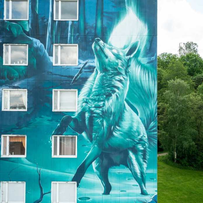 Close-up of Smug’s mural in Partille, Göteborg, created for the Artscape project. The mural, inspired by the Finnish tale of Revontulet, depicts a mythical fox with its head raised, symbolizing the legendary firefox that ignites the Northern Lights to guide a lost hiker. The blue and green tones evoke a wintry, forested landscape with snow and icy light, blending with the building’s structure. This piece is the tallest mural in Sweden and is rumored to be the tallest in Scandinavia.
