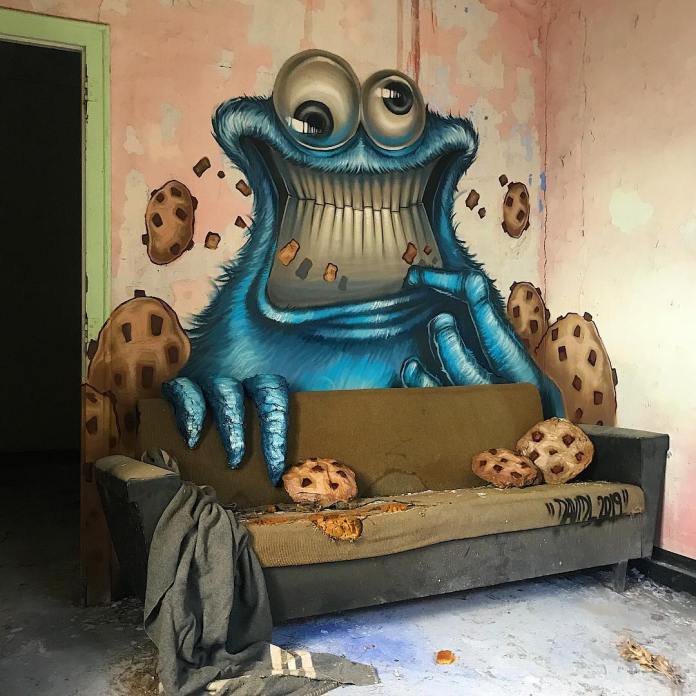 Post-graffiti artwork by DavidL featuring a monstrous, blue Cookie Monster eating cookies, painted on a distressed wall with a worn-out sofa in the foreground, located outside Barcelona, Spain.