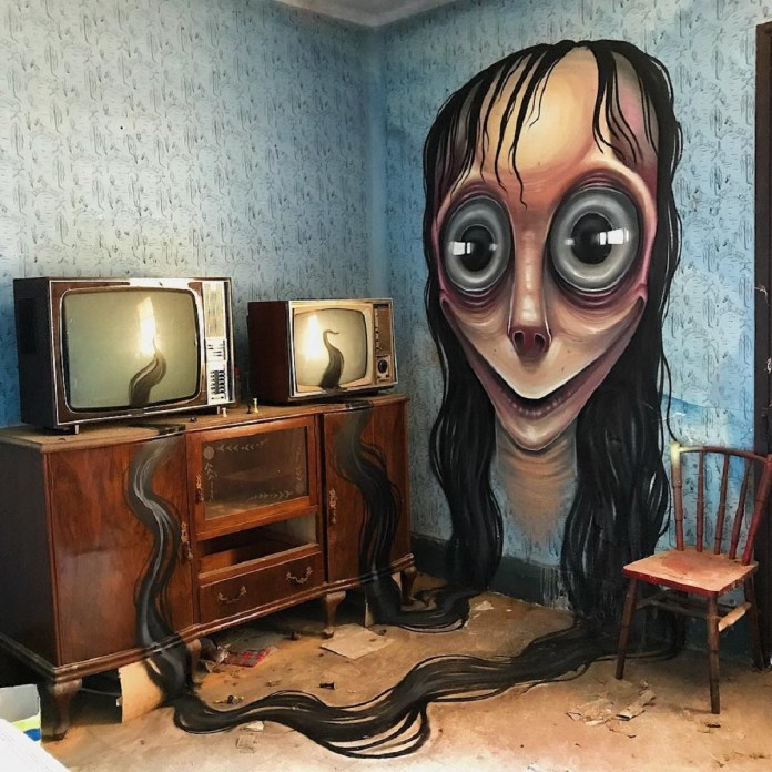 Post-graffiti artwork by DavidL featuring a creepy, wide-eyed figure inspired by Momo, with long black hair flowing across the floor, painted on a distressed wall beside vintage televisions, located outside Barcelona, Spain.