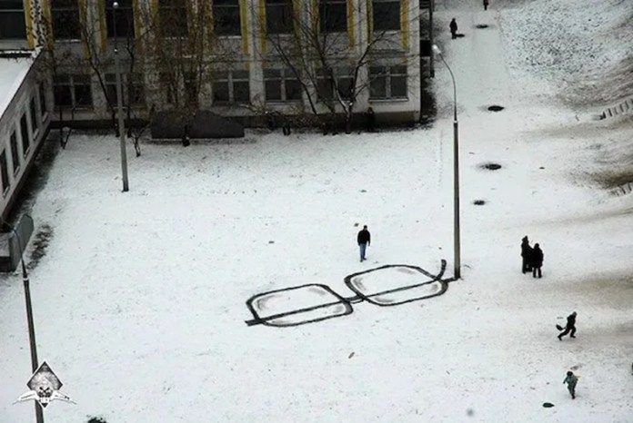 Street art featuring large black painted eyeglass frames on snowy ground, positioned so pedestrians appear as if walking through the glasses.