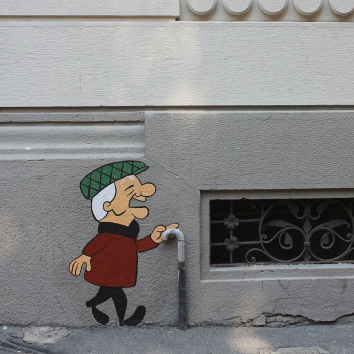 Cartoon mural of Mr. Magoo walking on a wall, using a real pipe as his cane, painted on a city building in Milan.