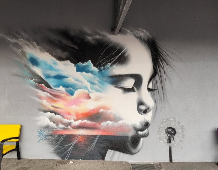 Mural by VYRUS showing a child in profile with eyes closed, hair dissolving into painted clouds and sunset sky, with a dandelion and golden light.