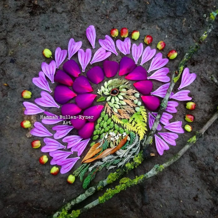 A vibrant ephemeral artwork by Hannah Bullen-Ryner, depicting a stylized bird surrounded by a circular, mandala-like arrangement of colorful petals. The bird is crafted from various natural materials, with its body formed from green leaves, ferns, and small pine needles, while an acorn cap or stone creates its eye. Surrounding the bird, bright pink and purple petals are arranged in a radiant circular pattern, accented by small red and green buds at the edges, creating a striking contrast against the earthy ground. This composition highlights the artist’s intricate layering and vibrant color choices, celebrating nature’s beauty in a harmonious, temporary form.