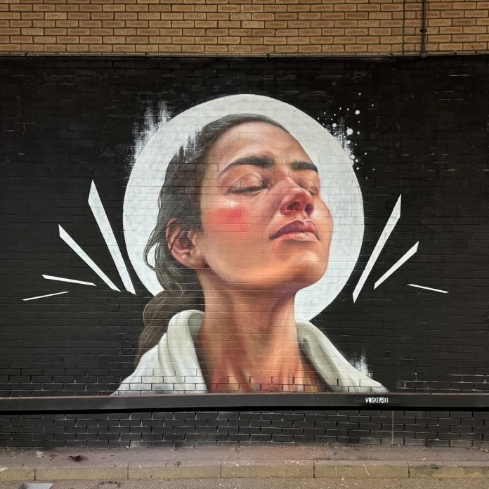 Portrait mural of a woman with eyes closed and head slightly raised, painted in realistic style with warm tones and a white circle behind her head.