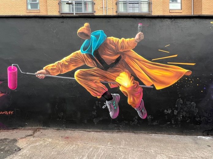 Mural in Glasgow showing a hooded, faceless figure in an orange coat leaping forward mid-air with a pink roller brush.