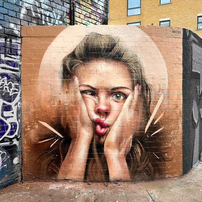 Mural of a blonde woman pressing her face with her hands into a squished expression, with soft tones and light effects on a textured brick wall.