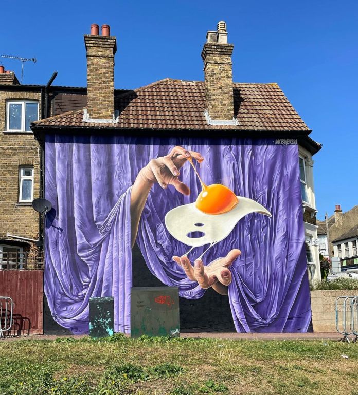 Large-scale mural in Shoreditch showing a hand lifting a fried egg from mid-air against a dramatic purple curtain backdrop that covers the entire building wall.