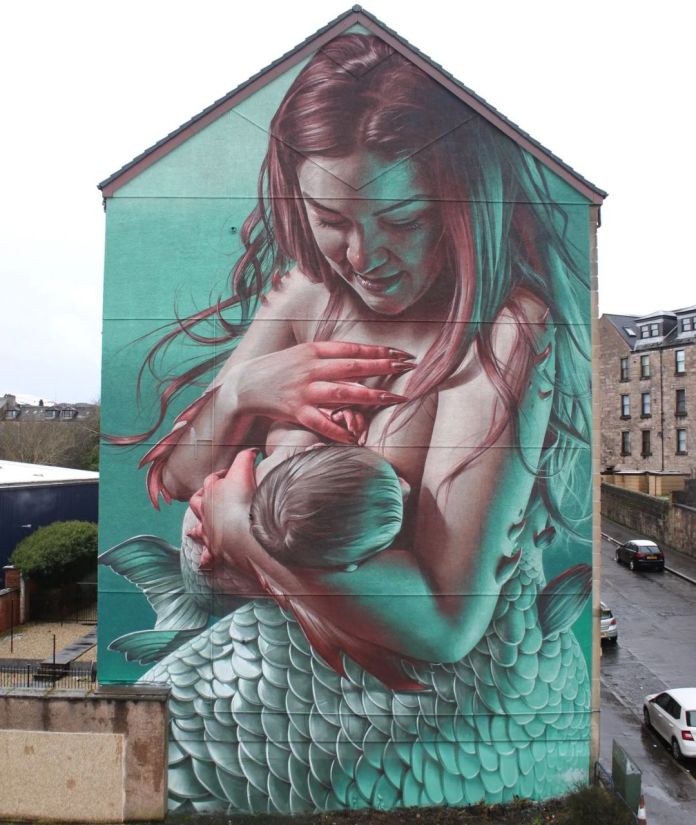 A photorealistic mural of a mermaid breastfeeding a baby, created by Smug One in Greenock, Scotland. The mermaid’s gentle expression and detailed fish-scale body create a visually striking statement advocating public acceptance of breastfeeding.