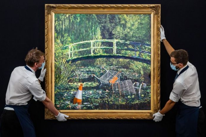 A reimagined Monet-inspired painting by Banksy, titled Show Me the Monet. The artwork depicts a serene garden scene with a Japanese-style bridge, but the pond is littered with shopping carts and an orange traffic cone, critiquing consumerism and environmental neglect. Two masked handlers carefully display the framed piece.