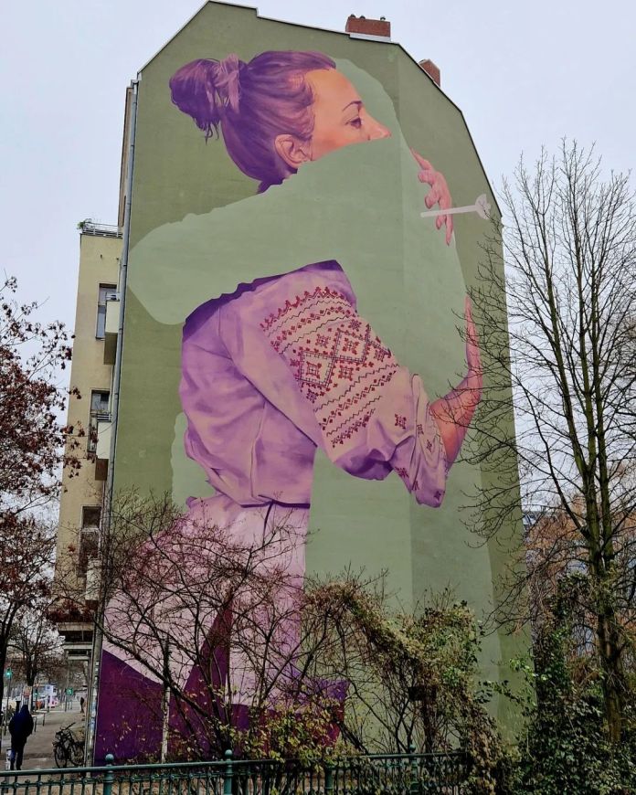 Large mural by Innerfields of a woman hugging a silhouette-shaped void painted the same green as the wall, symbolizing absence and emotional distance.