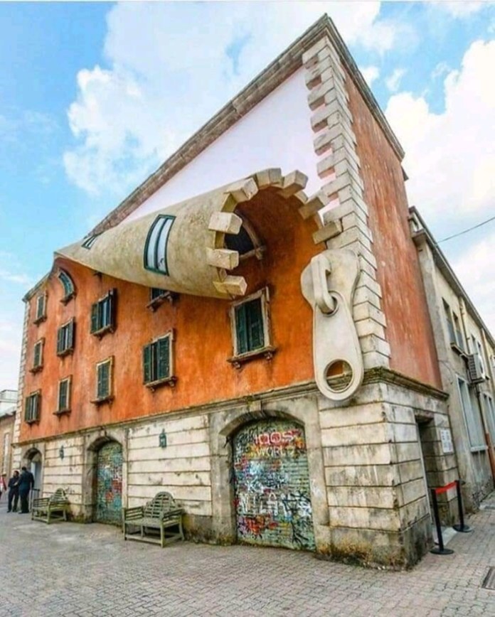 Building corner in Milan with a sculpted zipper peeling back the façade to expose windows behind, creating a surreal architectural illusion.
