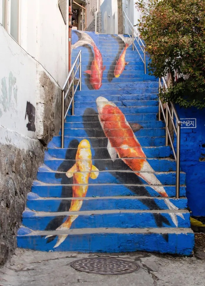 Blue-painted staircase featuring large koi fish murals that appear to swim upward, located in Ihwa Mural Village in Seoul, South Korea.