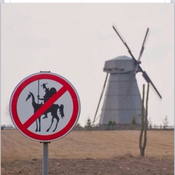 Comedic road sign with a red circle and slash over a silhouette of Don Quixote on horseback holding a lance. A windmill stands in the background, referencing the famous story.