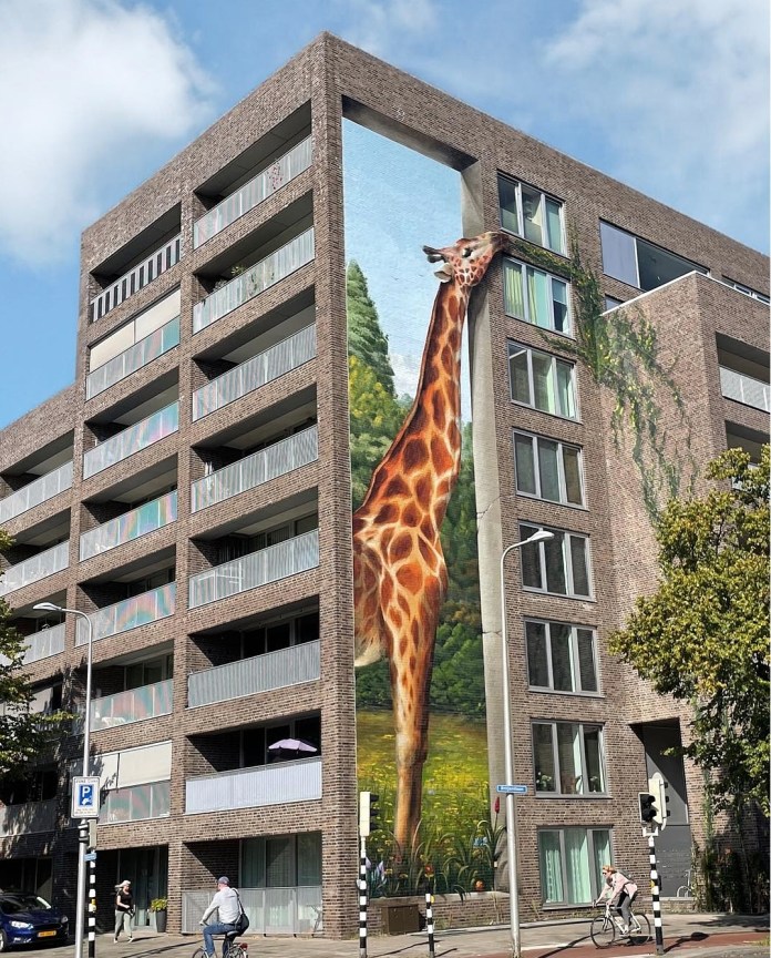Realistic mural of a giraffe on the corner of a modern apartment building in Utrecht, Netherlands. The giraffe's neck extends up the corner wall, appearing to eat leaves from a balcony garden, blending natural and architectural elements.