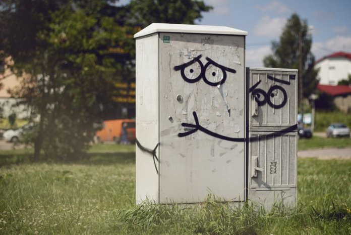 Two utility cabinets painted with cartoon faces and a hugging arm, turning them into affectionate characters. Found in Olsztyn, Poland.