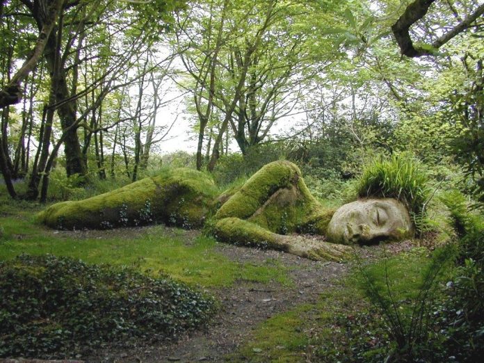 Sculpture of a reclining woman in a forest, covered in moss in Cornwall, UK.