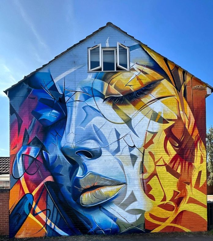 Abstract mural of a woman’s face in Swindon, UK, with closed eyes, painted in overlapping shapes of blue, orange, yellow, and white by Poster One.