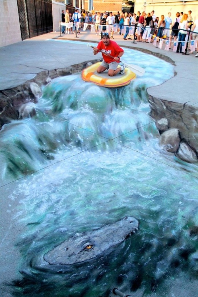 3D chalk street art in Charleston, West Virginia by Julian Beever showing a turbulent river with rocks and a crocodile, with a man kneeling in a real inflatable raft to complete the illusion.