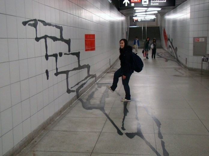 Optical illusion mural in a Toronto subway corridor by Panya Clark Espinal, showing painted stairs on the wall and floor that appear to descend into the ground as a person lifts their leg.