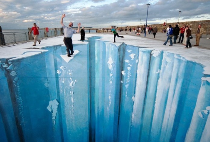3D pavement art in Ireland by Edgar Mueller, showing an icy crevasse that looks like a deep glacier crack, with people standing and pretending to fall into the opening.