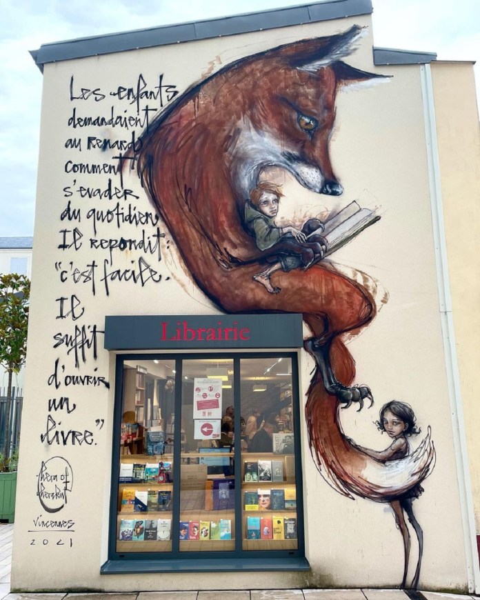 Street art by HERA in Vincennes, France, on a bookstore wall, showing a fox curled around a child reading, with French handwritten text encouraging escape through books.